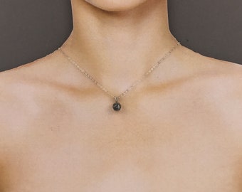 May include: A silver chain necklace with a small, dark gray, round pendant.