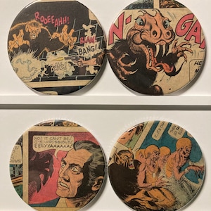 May include: Four round, colorful, vintage comic book style buttons with images of monsters and text. The buttons feature a werewolf, a creature with sharp teeth, a man with a surprised expression, and a group of monsters.