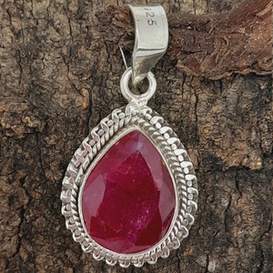May include: A teardrop-shaped pendant with a red gemstone set in a silver frame. The pendant has a silver bail with the number "925" stamped on it.