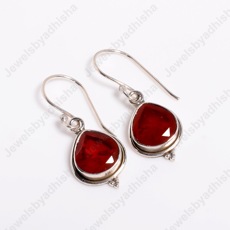 Peut inclure: Une paire de boucles d'oreilles pendantes en argent avec des gouttes de pierres pr&eacute;cieuses rouges. Les boucles d'oreilles ont un design simple et sont parfaites pour un usage quotidien.