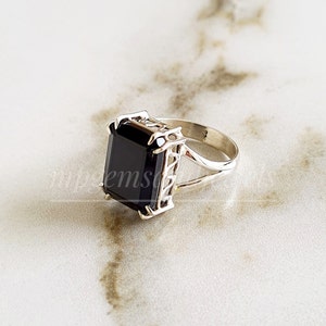 May include: A silver ring with a large, black, rectangular gemstone. The ring has a delicate, intricate design.