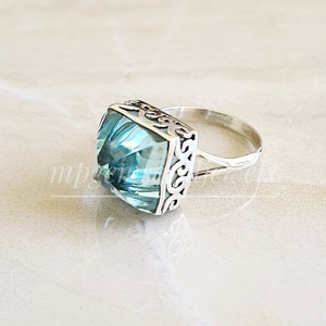 May include: A silver ring featuring a large, square, light blue gemstone set in a filigree design.