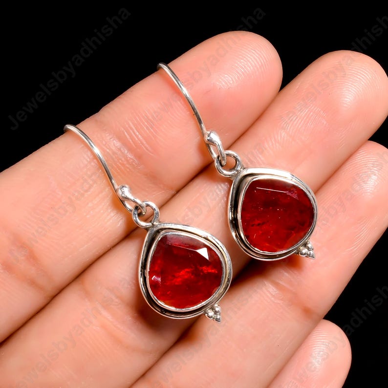 Peut inclure: Une paire de boucles d'oreilles pendantes en argent avec des gouttes de pierres pr&eacute;cieuses rouges. Les boucles d'oreilles ont une forme de larme et sont accentu&eacute;es de petites perles argent&eacute;es.