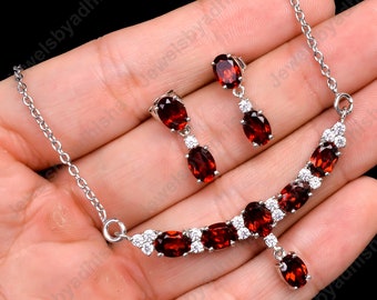 May include: A silver necklace and earrings set with red oval gemstones and clear round stones. The necklace has a pendant with a single red oval gemstone.