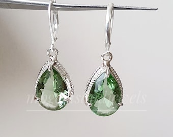 Peut inclure: Une paire de boucles d'oreilles pendantes en argent avec des pierres précieuses vertes en forme de poire. Les boucles d'oreilles ont un design délicat et orné.
