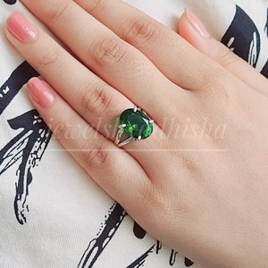 May include: A silver ring featuring a large, oval-shaped green gemstone. The ring is set with small, clear stones on the band.
