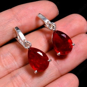 Può includere: Un paio di orecchini d'argento con pietre preziose rosse a forma di goccia. Gli orecchini hanno un design semplice e sono perfetti per l'uso quotidiano.