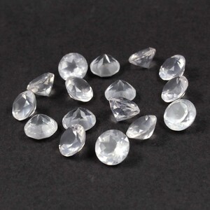 May include: A collection of 14 clear, faceted, round gemstones. The gemstones are scattered on a black surface.
