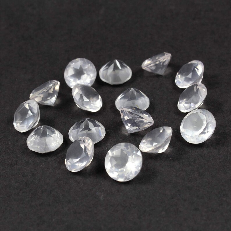 May include: A collection of 14 clear, faceted, round gemstones. The gemstones are scattered on a black surface.