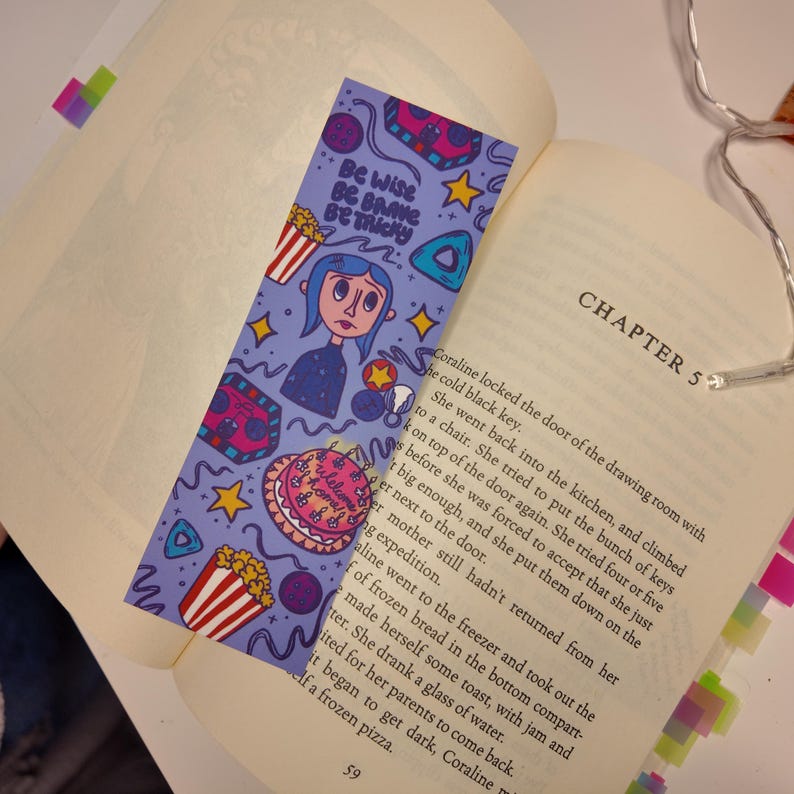 Może przedstawiać: Fioletowa zakładka do książki z kresk&oacute;wkową ilustracją dziewczyny z niebieskimi włosami i napisem "Be Wise, Be Brave, Be Tricky". Zakładka zawiera r&oacute;wnież obrazy popcornu, ciasta i gwiazd. Zakładka jest umieszczona w otwartej książce.