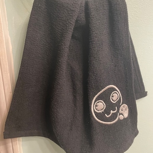 May include: Black kitchen towel with a white embroidered cartoon face and paw print.