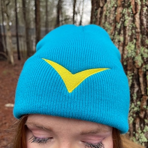 Könnte beinhalten: Eine türkisblaue Strickmütze mit einem gelben Chevron-Muster.