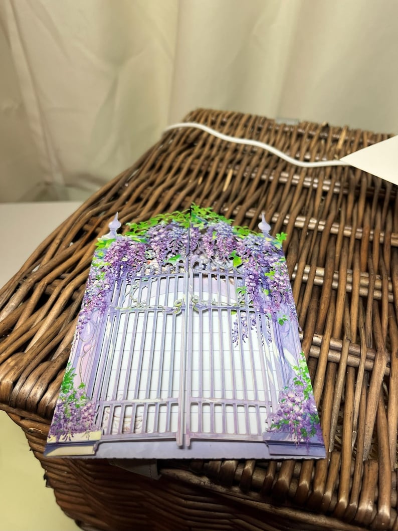 May include: A decorative card featuring a purple gate adorned with wisteria flowers. The gate is detailed with vertical bars and is surrounded by cascading purple blossoms. The card is set against a woven basket background, creating a charming, floral theme.