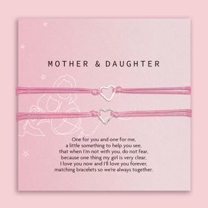 May include: Two pink string bracelets with silver heart charms, displayed on a pink card with the words "MOTHER & DAUGHTER." The card also includes a poem about love and togetherness. A thoughtful gift.