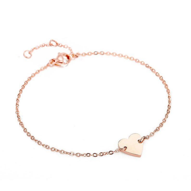 May include: Rose gold bracelet featuring a delicate chain and a heart-shaped charm. The bracelet has an adjustable length and a lobster clasp closure. The heart charm is smooth and polished, adding a touch of elegance to the jewelry.
