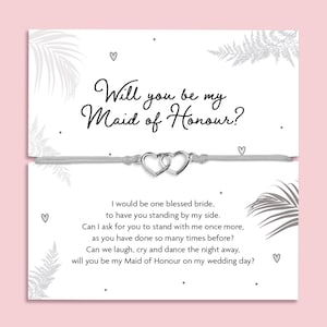 May include: A silver-toned heart charm bracelet with a light grey cord, presented on a card. The card reads "Will you be my Maid of Honour?" with a poem. The background is white with fern and heart details.