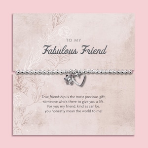 May include: A silver-toned beaded bracelet featuring a small flower charm and a heart charm, displayed on a rectangular card with the text "TO MY Fabulous Friend" and a poem about friendship, decorated with light-coloured line art floral illustrations.