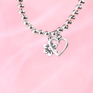 May include: A silver bracelet with a heart and flower charm. The bracelet is made of small silver beads and the charm is attached to the bracelet with a silver loop.