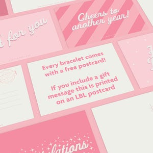 May include: A collection of pink and white postcards with various greetings. The cards feature phrases like "Just for you," "Cheers to another year," and "Happy Birthday." One card states, "Every bracelet comes with a free postcard!"