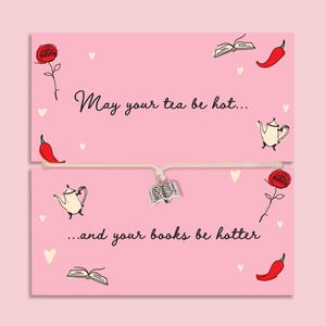 Può includere: Un biglietto rosa con la scritta "May your tea be hot... and your books be hotter." Il biglietto presenta illustrazioni di una rosa, un peperoncino, una teiera, un libro aperto e piccoli cuori. Un braccialetto con un ciondolo a forma di libro è al centro.