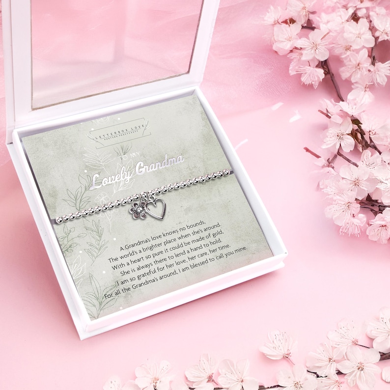 Silver beaded bracelet with heart and flower charms, presented in a white gift box with a sentimental card reading "Lovely Grandma." The card features a heartfelt poem and floral accents, perfect for celebrating a cherished grandmother.