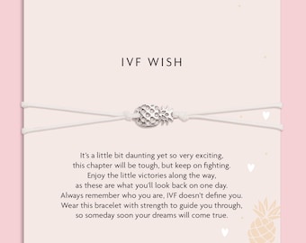 May include: A white string bracelet with a silver pineapple charm. The bracelet is displayed on a card with the text "IVF WISH" and inspirational text about IVF. The background is a light pink color.