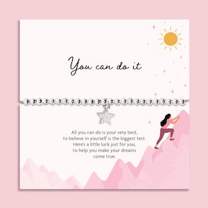 May include: A pink card with the text "You can do it" and a silver beaded bracelet with a star charm. The card also features an illustration of a person climbing a mountain and inspirational text.