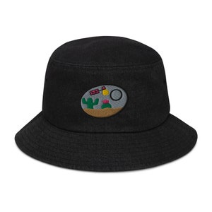 May include: Black bucket hat with a desert scene embroidered on the front. The scene includes a cactus, a flower, a sun, and a satellite.