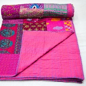 May include: A pink kantha quilt with a patchwork design featuring various shades of pink, purple, and teal. The quilt is made from recycled saris and is hand-stitched with intricate embroidery.