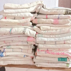 May include: A stack of white cotton blankets with colorful woven patterns. The blankets are folded and stacked neatly on a wooden surface.