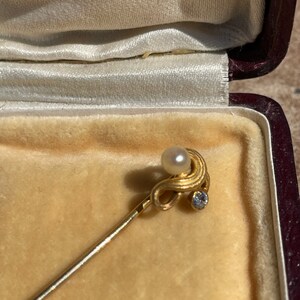 May include: A gold-toned stick pin with a pearl and a small diamond-like stone. The pin is displayed inside a velvet-lined jewelry box with the word "LARNE" embossed on the inside of the lid.