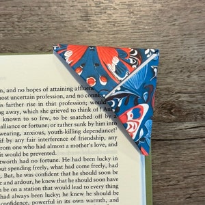 May include: A blue and red patterned bookmark with a triangular shape. The bookmark is folded in half and has a white edge.