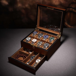 May include: A wooden watch box with a glass top, showcasing multiple wristwatches with various colored faces. The box has a drawer with jewelry. The watches are displayed in individual compartments, and the box is set against a dark background.