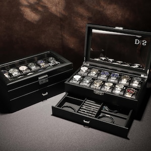 Könnte beinhalten: Schwarze Lederuhrenbox mit zwei Schubladen und einer Glasplatte. Die Box ist mit 20 Armbanduhren gefüllt. Die Box trägt den Text "D|2" auf der Oberseite.