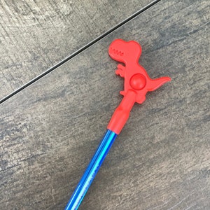 May include: A blue and red pen with a red dinosaur-shaped top. The dinosaur has a spinning ball on its back.