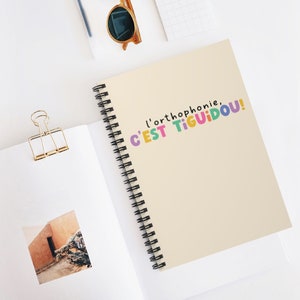 May include: A cream-coloured spiral notebook with the text "l'orthophonie, C'EST TIGUIDOU!" in colourful letters.