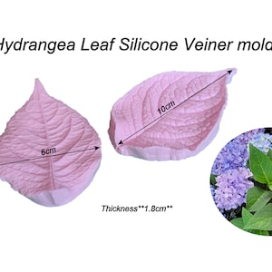May include: Two pink silicone hydrangea leaf molds with detailed veining, measuring 6cm and 10cm in length. The thickness is 1.8cm. The image also includes a photo of a hydrangea flower and the text "Hydrangea Leaf Silicone Veiner molds".