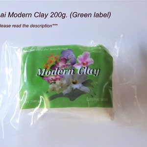 May include: A white package of Thai Modern Clay, labeled in green with a floral design. The package contains 200 grams of clay.