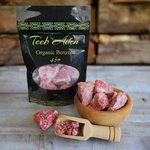 Op de afbeelding: Een zwarte verpakking van "Teeb Aden Organic Benzoë" met een transparant venster met roze-rode harsbrokken. Een houten kom en lepel bevatten meer hars. De verpakking geeft 50 g aan.