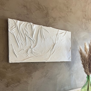 May include: White textured wall art with a raised, abstract design. The art is hanging on a brown wall with a white trim.