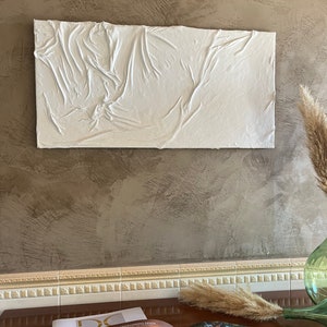May include: White textured wall art with a raised, wrinkled surface. The art is hanging on a brown textured wall.