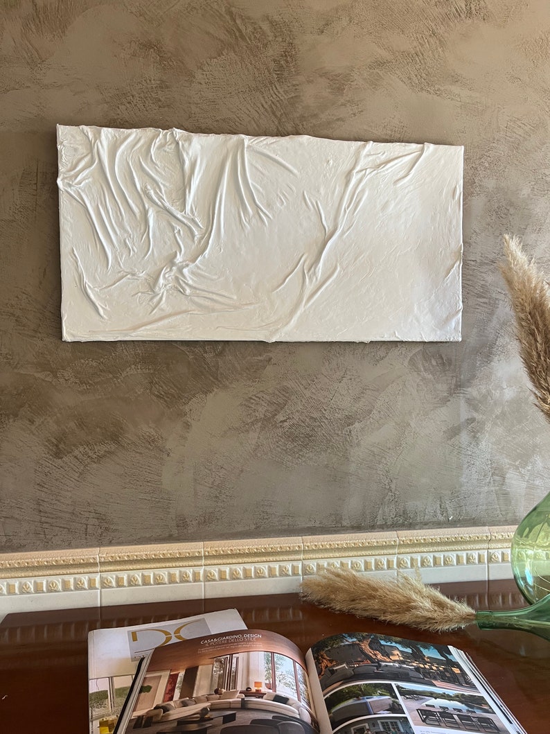 May include: White textured wall art with a raised, wrinkled surface. The art is hanging on a brown textured wall.