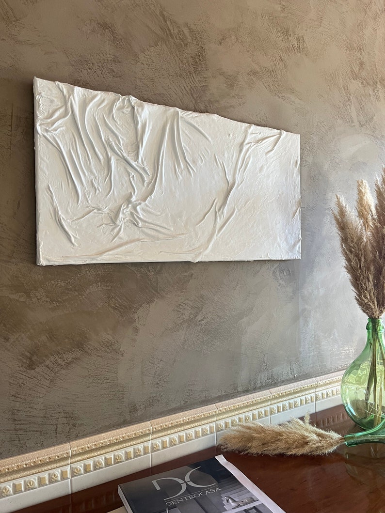 May include: White textured wall art with a raised, abstract design. The art is hanging on a brown wall with a white trim.