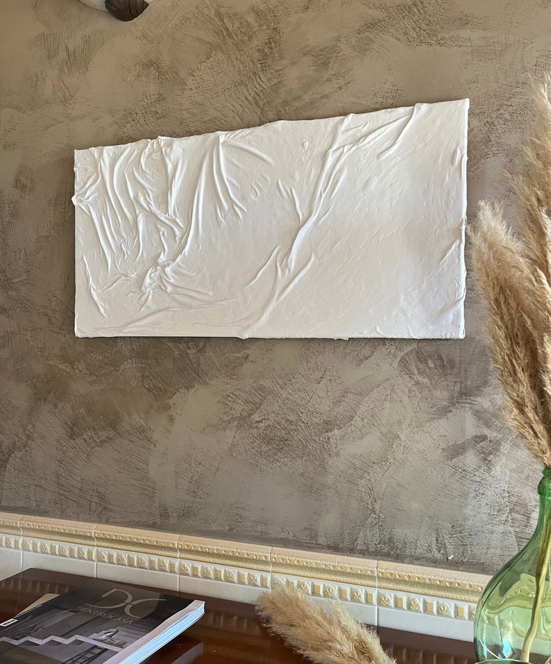May include: White textured wall art with a raised, wrinkled surface. The art is hanging on a brown wall with a white trim.