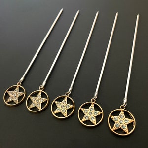 May include: Set of six silver cocktail sticks with gold star-shaped charms. Each charm is adorned with clear rhinestones.