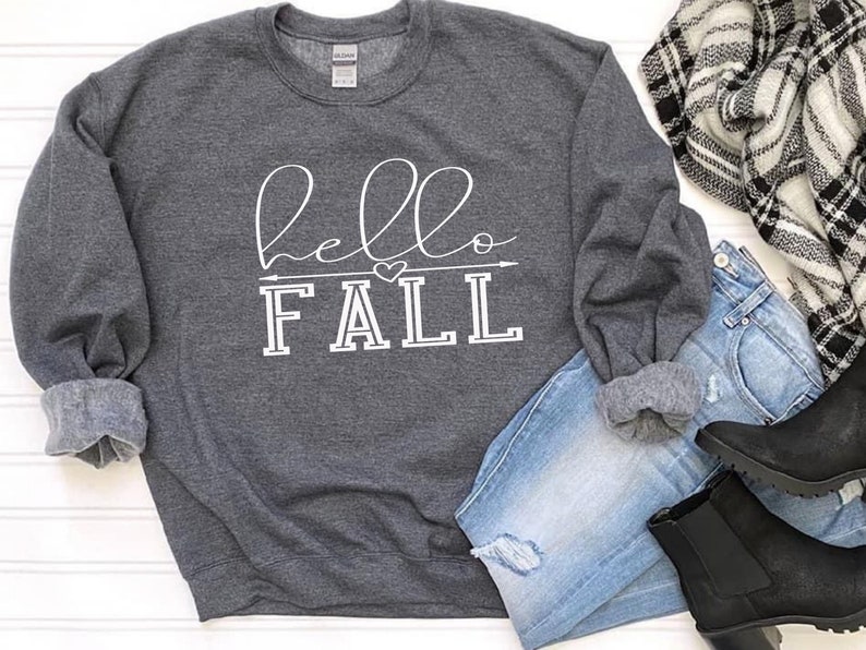 以下が含まれることがあります： 白い文字で「hello fall」と書かれたグレーのスウェットシャツ。小さなハートと矢印のグラフィックが描かれている。