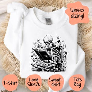 May include: A white t-shirt featuring a black and white illustration of a skeleton reading a book surrounded by flowers. The text "Unisex sizing!" is in a white circle in the top right corner of the image. The text "T-Shirt", "Long Sleeve", "Sweat-shirt", and "Tote Bag" are in white circles at the bottom of the image.