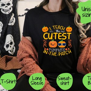 May include: Black t-shirt featuring a graphic of pumpkins wearing sunglasses and the text "I teach the cutest pumpkins in the patch". The shirt is available in t-shirt, long sleeve, sweatshirt, and tote bag styles.
