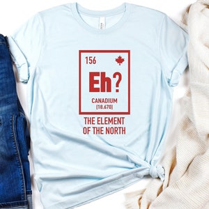 May include: Light blue t-shirt with a red graphic of a periodic table element. The element is labeled "Eh?" with the text "Canadium [18.670]" and "The Element of the North".