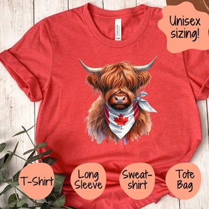 May include: Red t-shirt with a graphic of a Highland cow wearing a bandana with the Canadian flag. The text "Unisex sizing!" is in a speech bubble above the cow. The t-shirt is available in a variety of styles, including a long-sleeve t-shirt, a sweatshirt, and a tote bag.